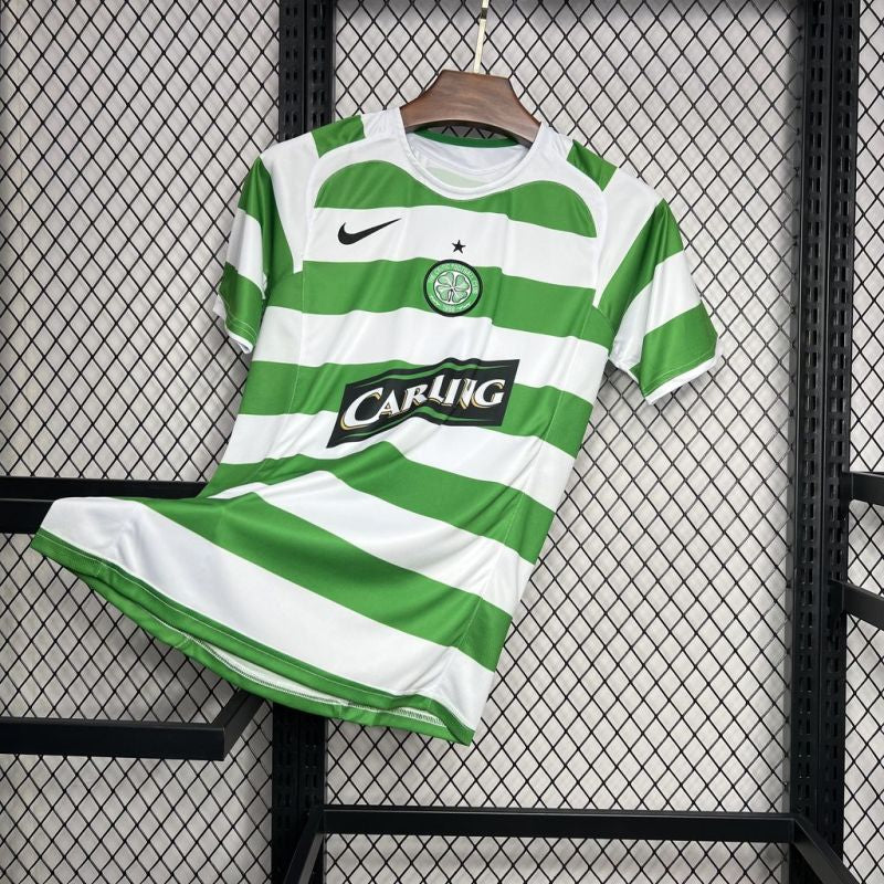 Celtic FC 2005-2006 home football shirt with green and white hoops, Carling sponsor logo, Nike logo, and club crest, hanging on a wooden hanger against a mesh background.