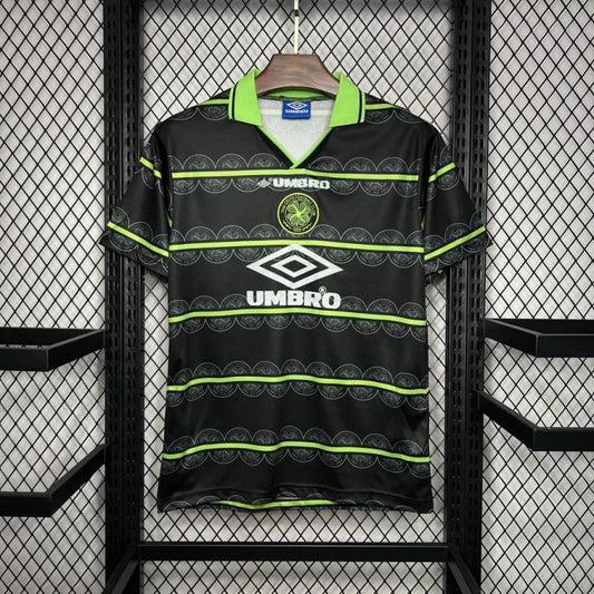 Celtic FC retro-style football shirt by Umbro with green and black horizontal patterns, hanging on a display rack.