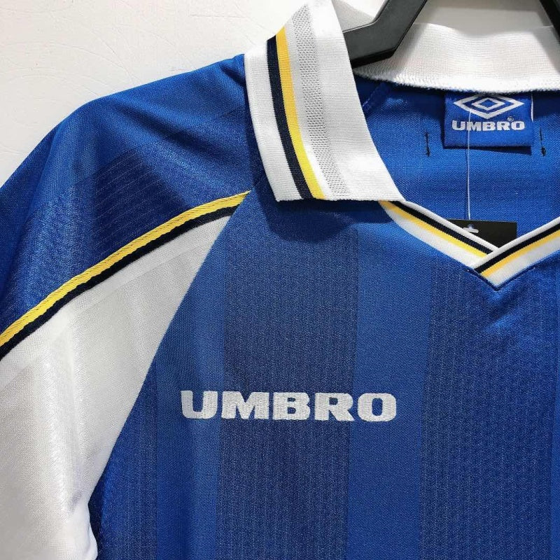Close-up of the upper section of a Chelsea FC 1999 Umbro home shirt, showing the collar, Umbro logo, and yellow-black trim detail.