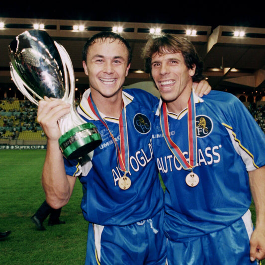 Two Chelsea FC players celebrating on the pitch wearing the 1999 Umbro home shirt with Autoglass sponsor, holding a trophy and medals after a match.