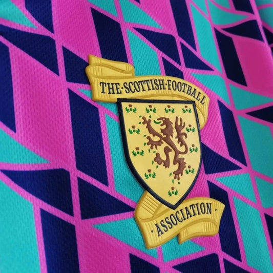 Close up view of a retro-style 1988 Scotland football shirt by Umbro, featuring a vibrant geometric pattern in pink, teal, and navy, with the Scottish Football Association crest on the chest.