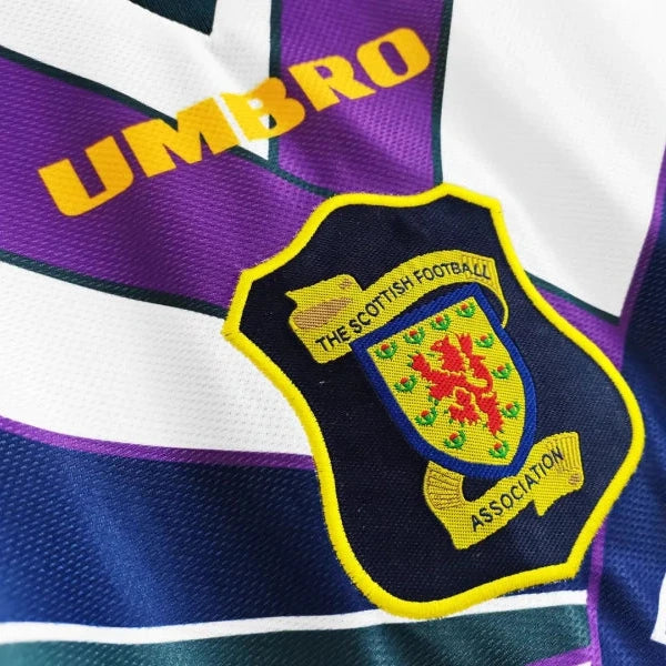 Close up view of a white 1994 Scotland football shirt by Umbro, featuring bold purple and navy geometric patterns, a collared neckline, and the Scottish Football Association crest on the chest.