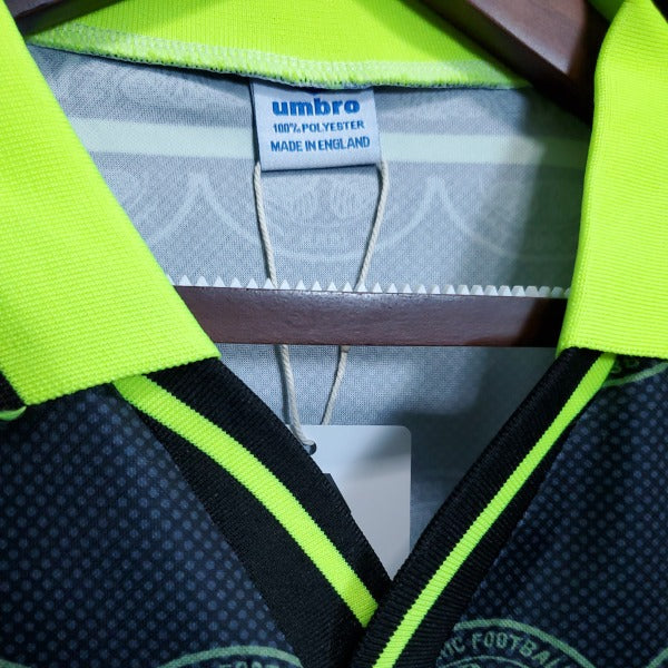 Close up of a 1999 Celtic FC football shirt featuring the Umbro logo and neon yellow horizontal stripes on a dark background.